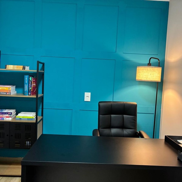 Sala de atendimento com escrivaninha, poltrona e estante de livros